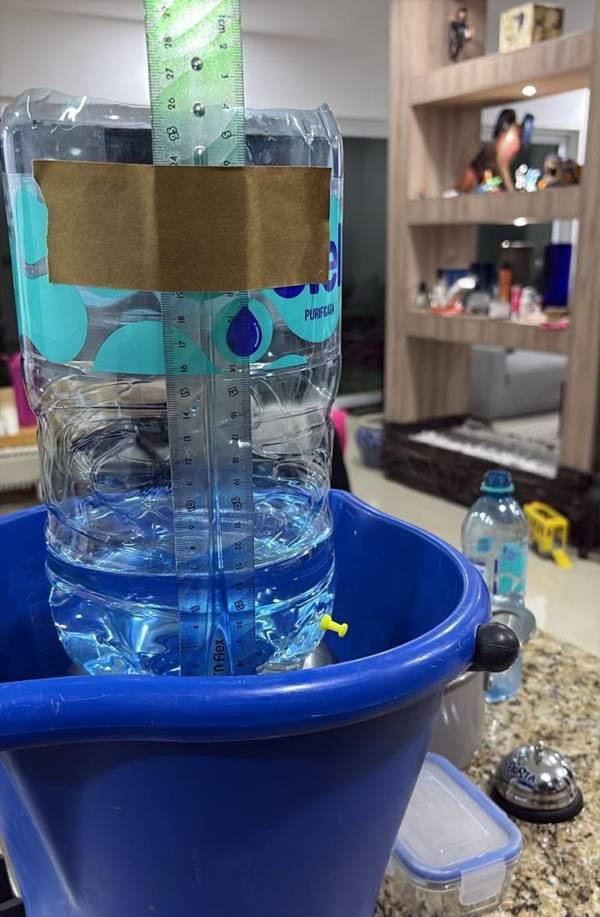 Garrafón con una regla pegada por fuera y una chinche amarilla tapando un agujerito, dentro de una cubeta